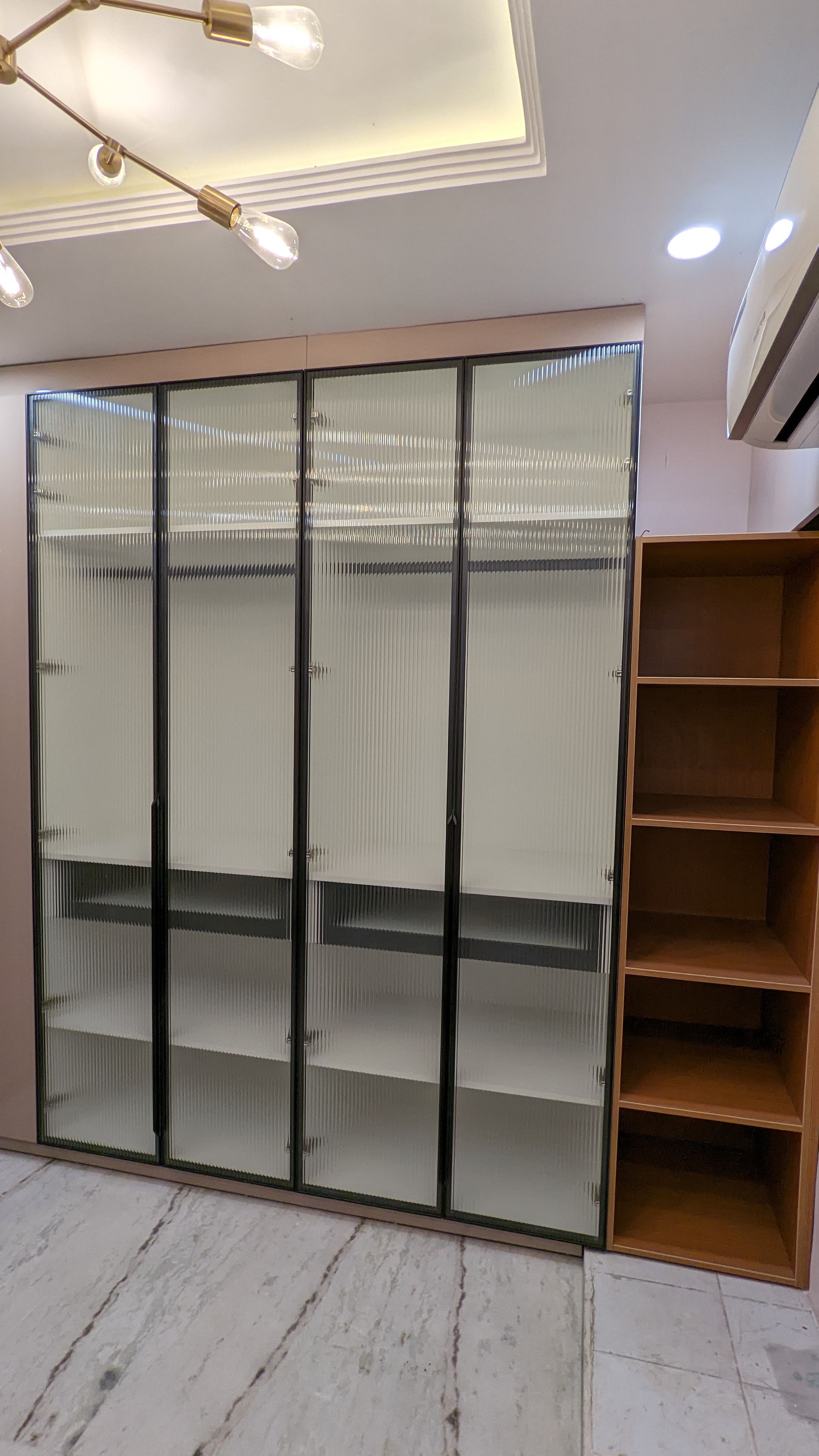 Walk-in wardrobe with fluted frosted-glass shutters and open wood shelving
